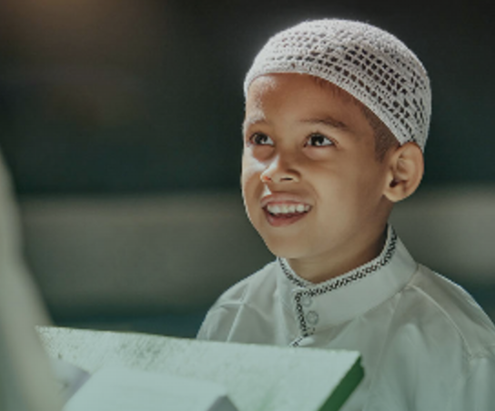 Young boy in a prayer cap holding the Qur’an